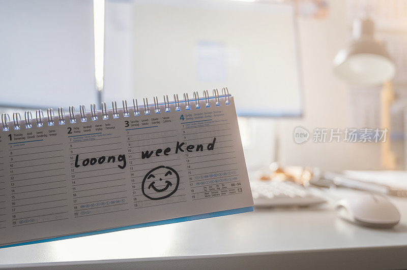 Calendar with the long weekend note in front of a desk with a computer